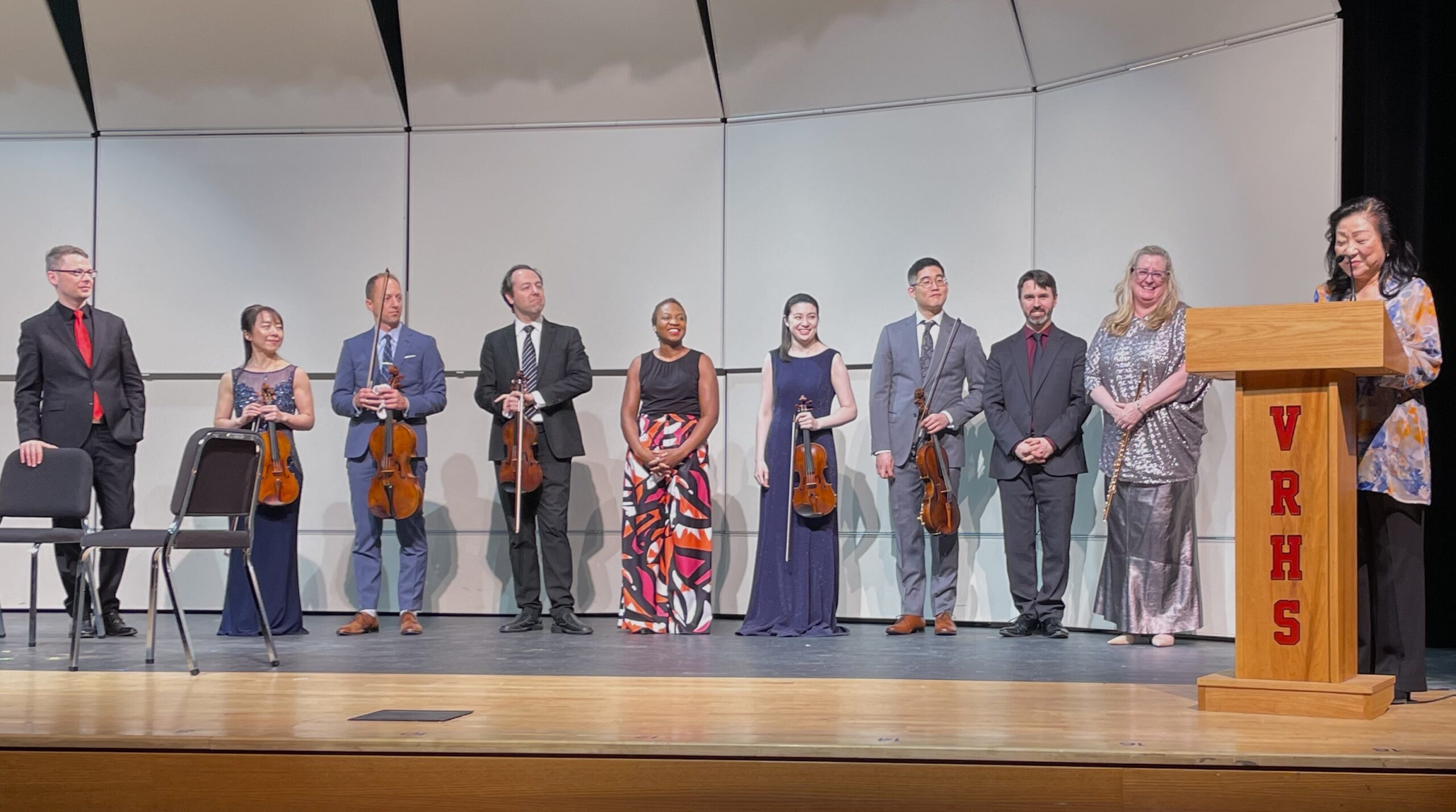 Retiring Artistic Director Mihae Lee at podium with incoming AD Tara Helen O'Connor and 8 returning artists alumni